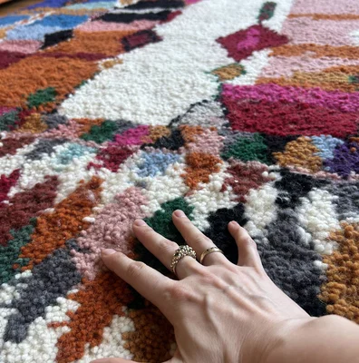 Hand feeling the raised wool texture and bright geometric pattern of a Moroccan rug